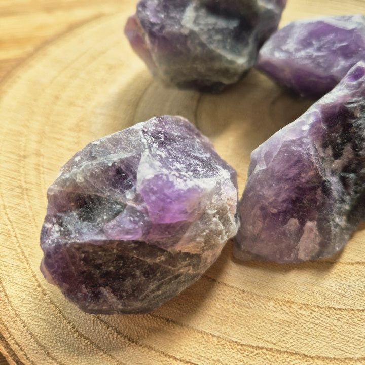 Pierre brute d’améthyste violette (~6 cm), cristaux naturels non polis, teintes lavande à pourpre, posée sur fond blanc, symbole sérénité et protection.